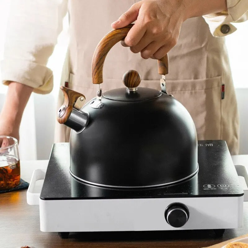 Bouilloire à sifflet inox 3L, design moderne, noire, sur cuisinière à induction. Élégante, sécurité optimale.