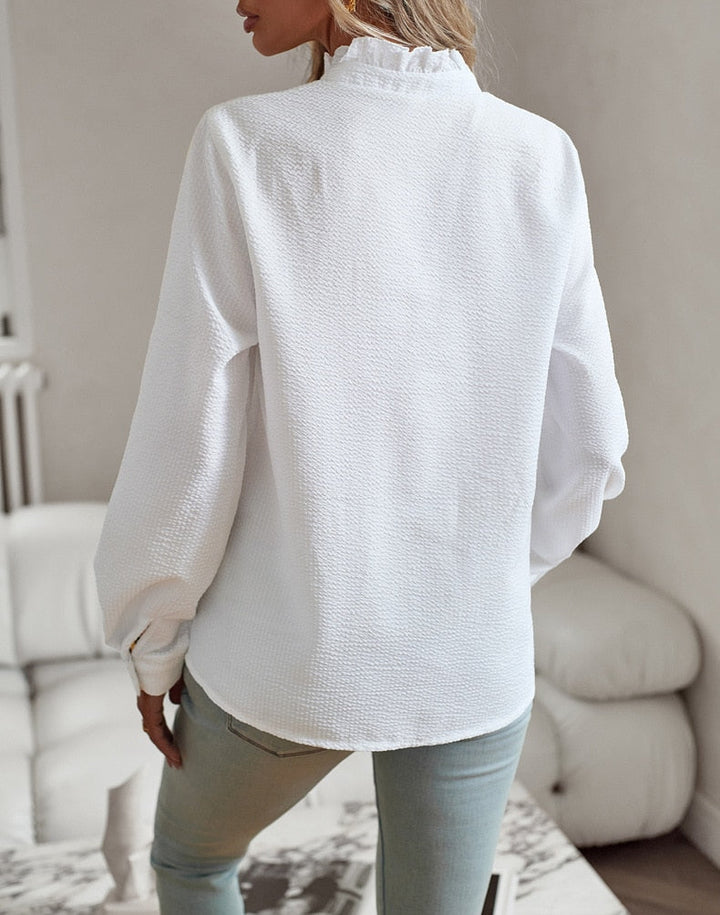 Chemisier femme élégant Lisbeth, col à manchettes distinctif sur fond clair, manches longues et tissu luxueux.