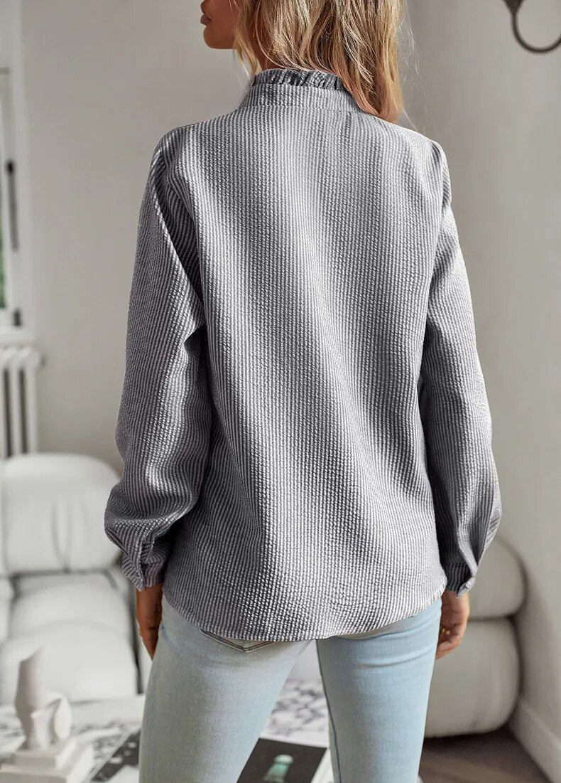 Chemisier femme élégant Lisbeth, col à manchettes distinctif sur fond clair, manches longues et tissu luxueux.