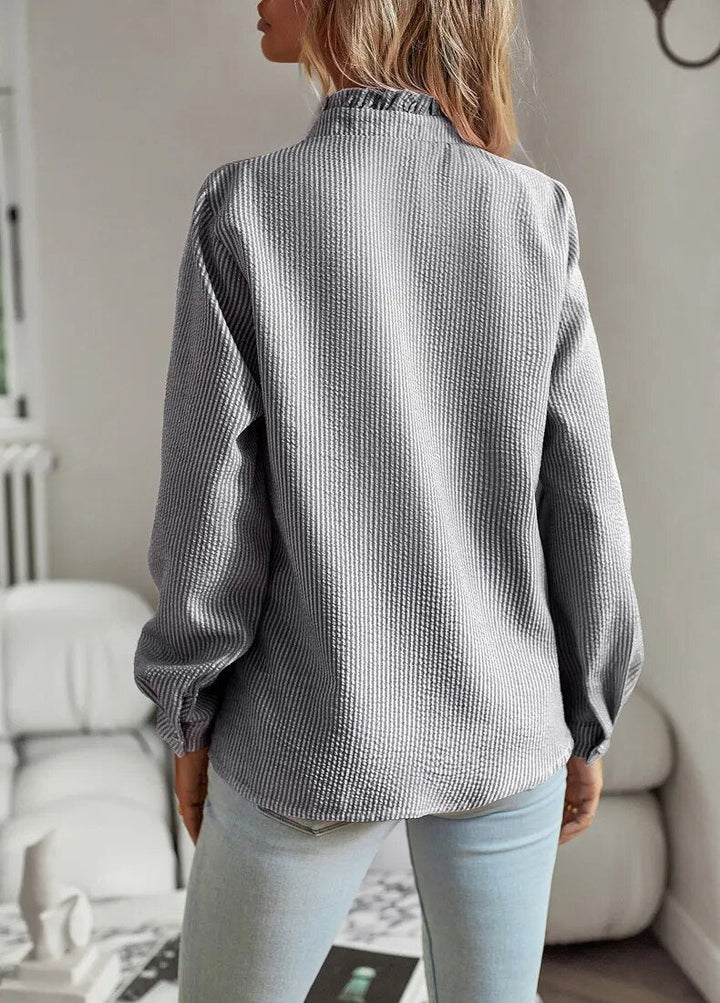 Chemisier femme élégant Lisbeth, col à manchettes distinctif sur fond clair, manches longues et tissu luxueux.