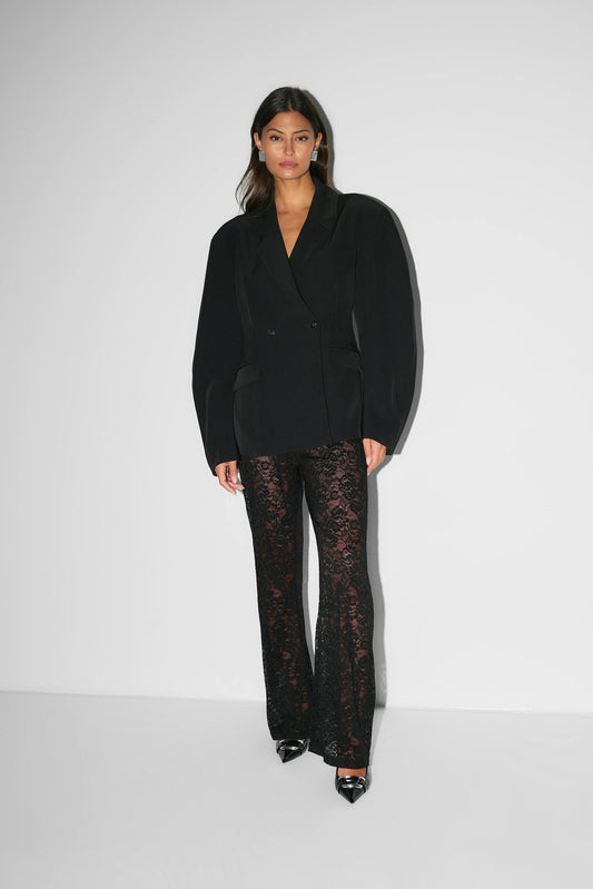 Pantalon évasé à taille haute en dentelle noire, silhouette élancée, matière florale transparente pour allure glamour.