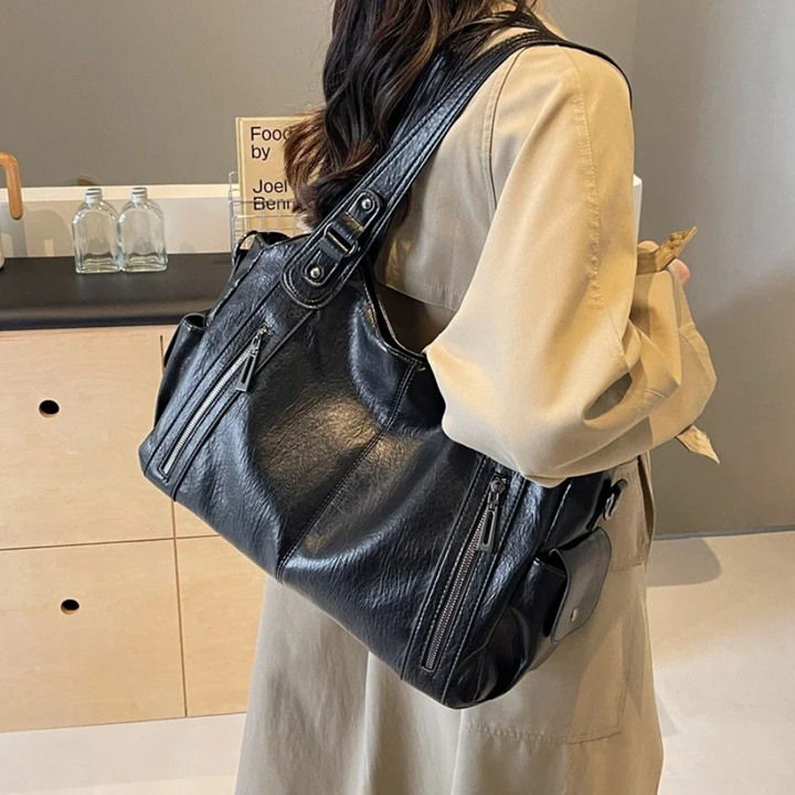 "Sac Amber en cuir végétal marron avec bandoulière, détails métalliques et poches, design élégant et spacieux pour femme."