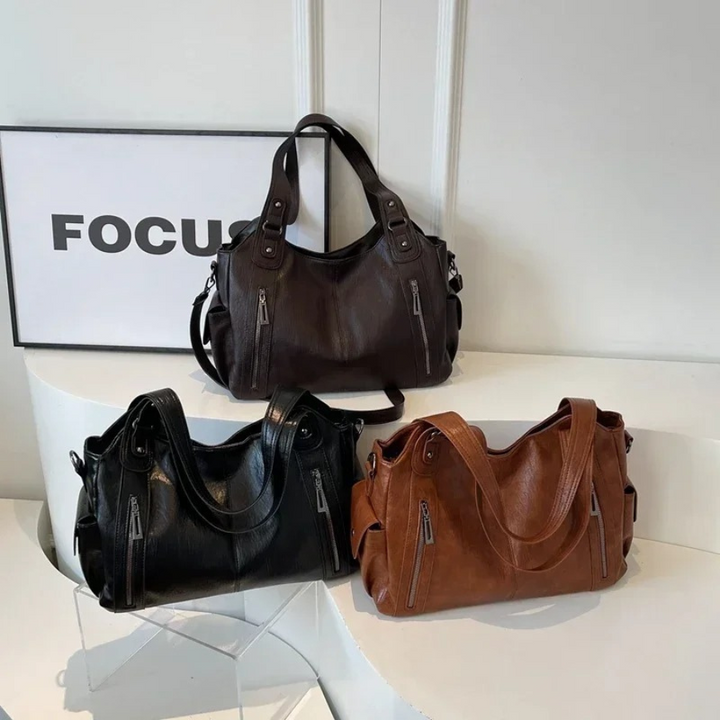 "Sac Amber en cuir végétal marron avec bandoulière, détails métalliques et poches, design élégant et spacieux pour femme."