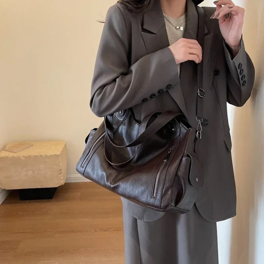 "Sac Amber en cuir végétal marron avec bandoulière, détails métalliques et poches, design élégant et spacieux pour femme."