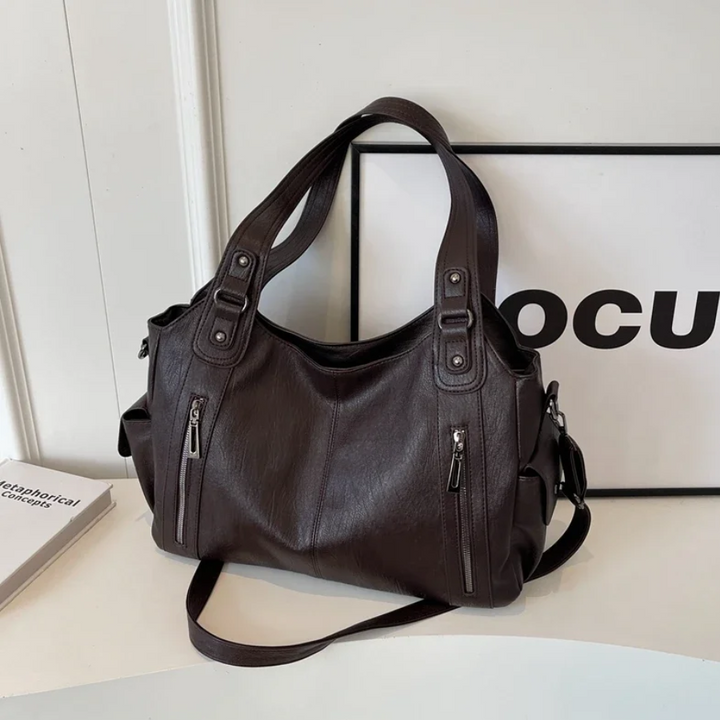 "Sac Amber en cuir végétal marron avec bandoulière, détails métalliques et poches, design élégant et spacieux pour femme."