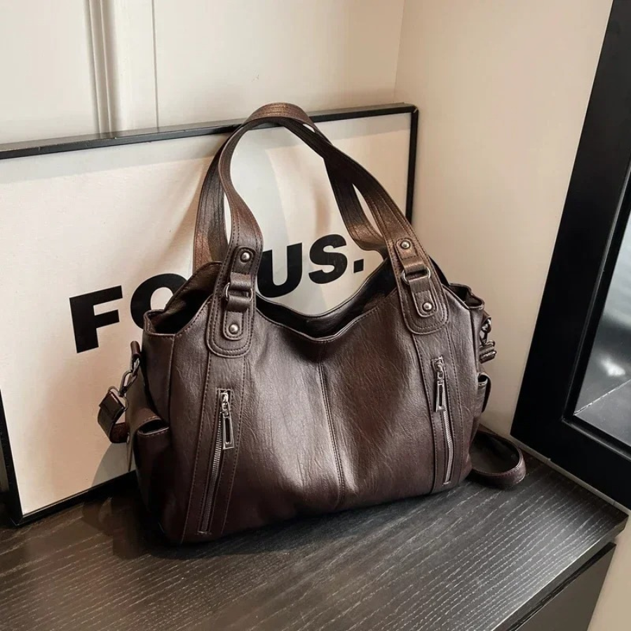 "Sac Amber en cuir végétal marron avec bandoulière, détails métalliques et poches, design élégant et spacieux pour femme."