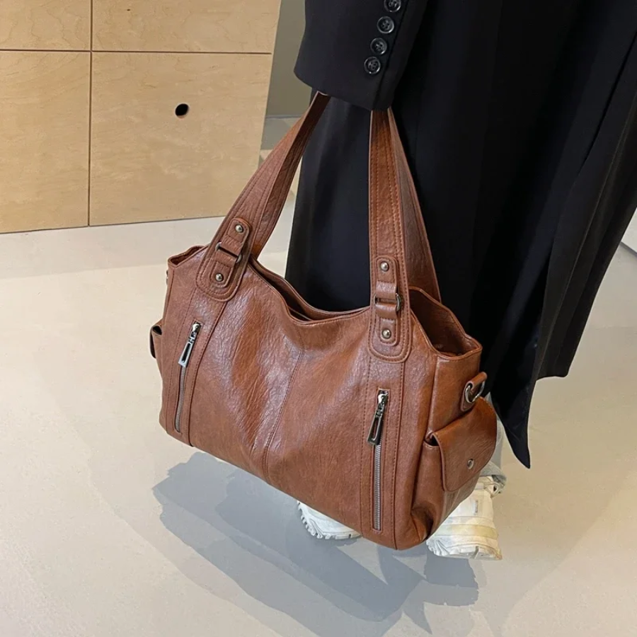 "Sac Amber en cuir végétal marron avec bandoulière, détails métalliques et poches, design élégant et spacieux pour femme."