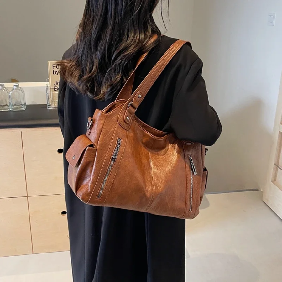 "Sac Amber en cuir végétal marron avec bandoulière, détails métalliques et poches, design élégant et spacieux pour femme."