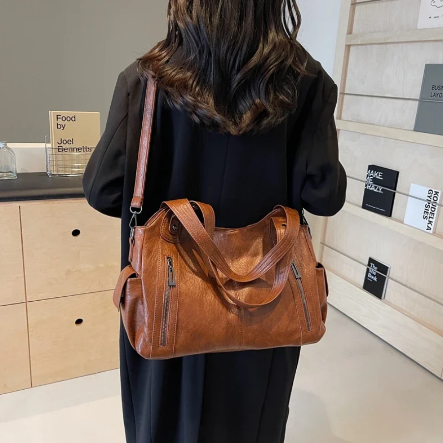"Sac Amber en cuir végétal marron avec bandoulière, détails métalliques et poches, design élégant et spacieux pour femme."