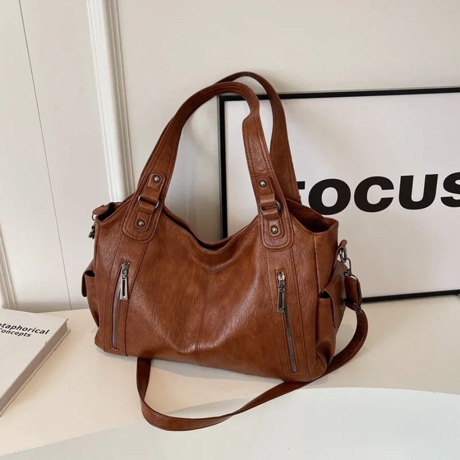 "Sac Amber en cuir végétal marron avec bandoulière, détails métalliques et poches, design élégant et spacieux pour femme."