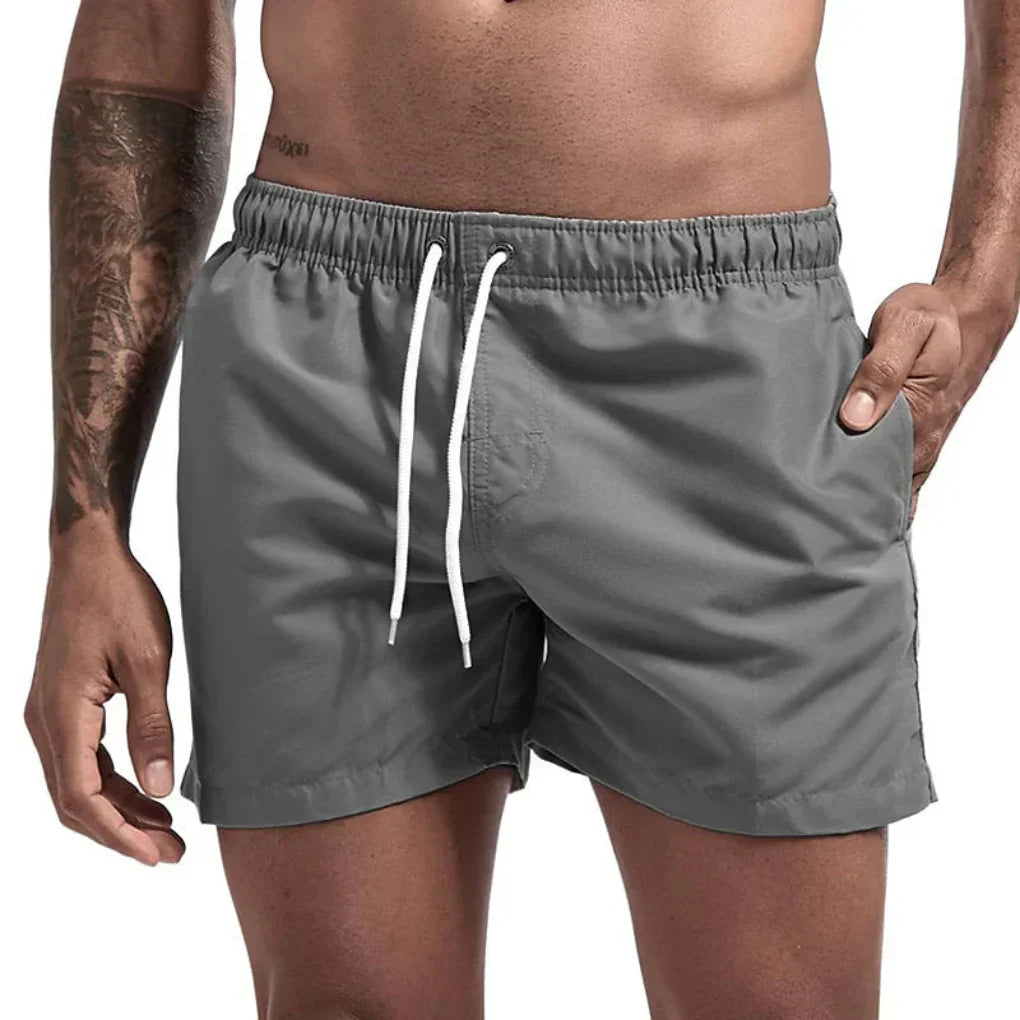 "Short de bain homme bleu clair, séchage rapide, doublure en mesh, poches latérales et arrière, ceinture élastique."